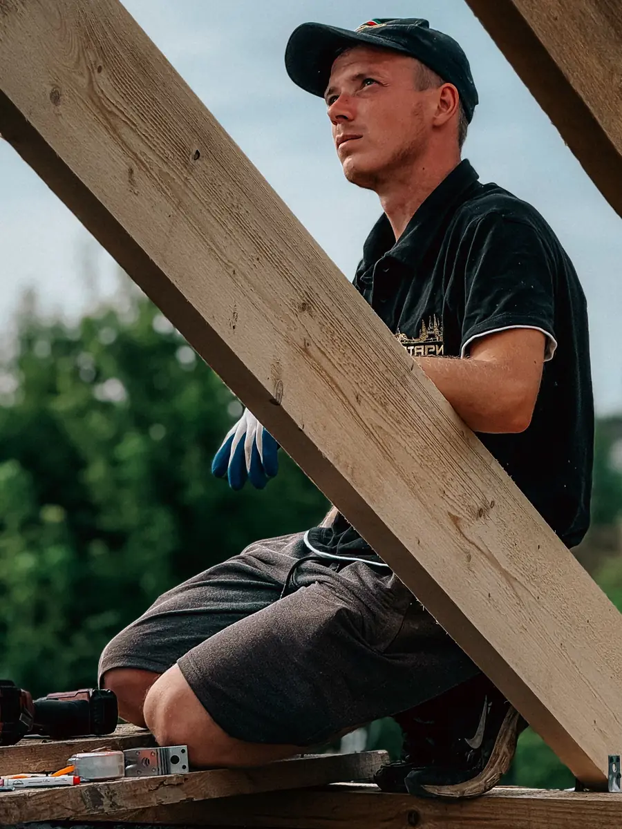 Zimmermann sitzt auf dem neuen Dachstuhl zwischen den Sparren